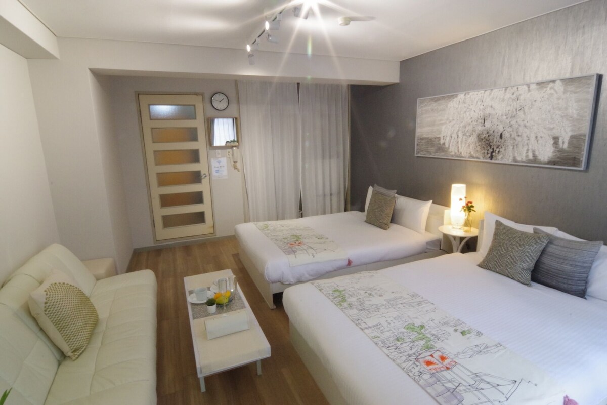 A hotel room with two beds, a sofa, a small table with a vase of flowers, and a painting on the wall.