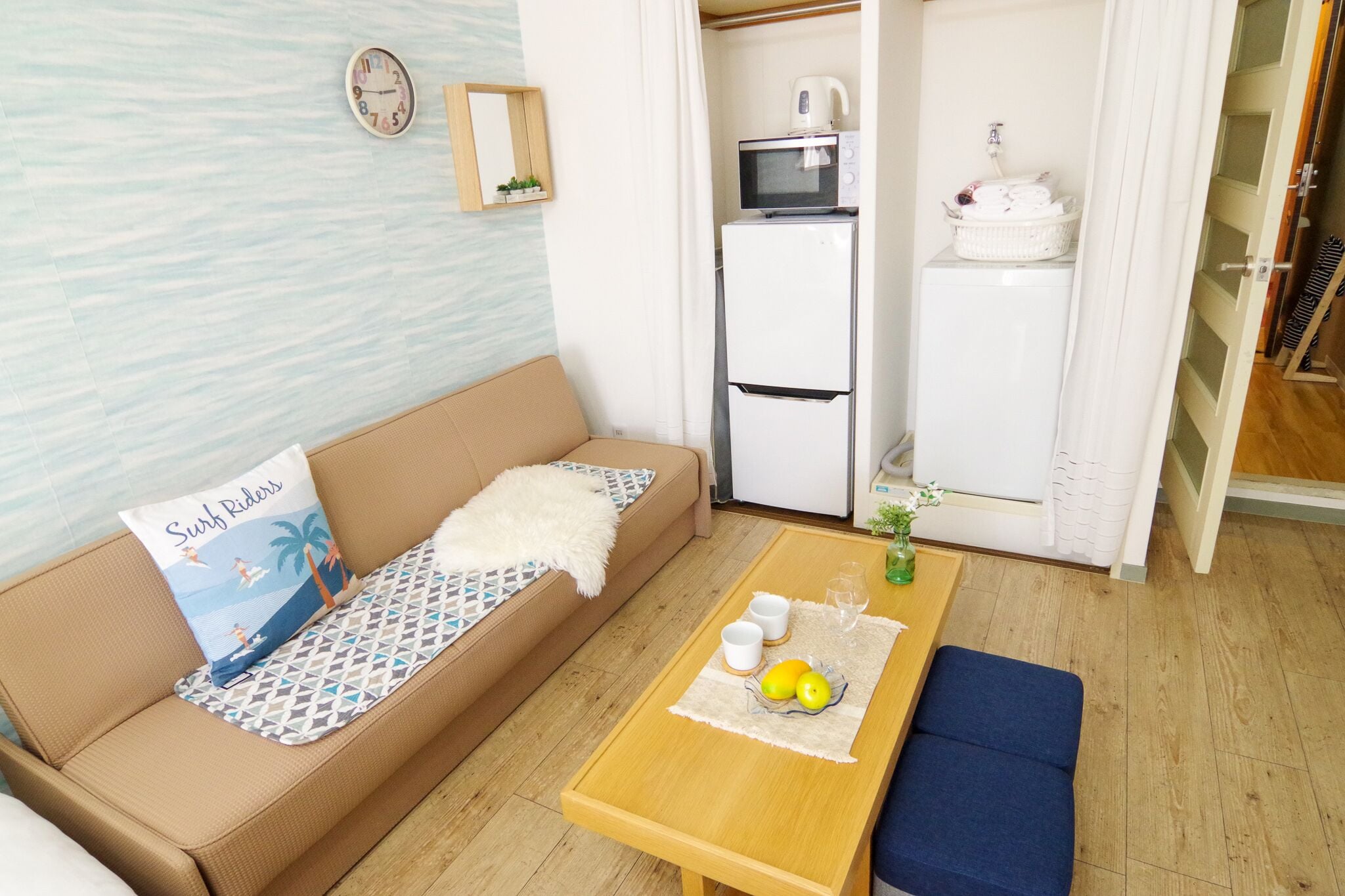 A compact living space with a sofa, a small table with cups and lemons, a microwave, and a refrigerator.