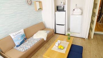 A compact living space with a sofa, a small table with cups and lemons, a microwave, and a refrigerator.