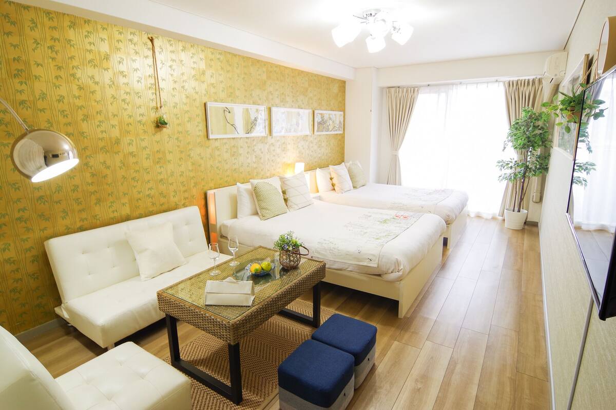 A hotel room with a sofa, a bed, a small table with a glass top, and a potted plant.