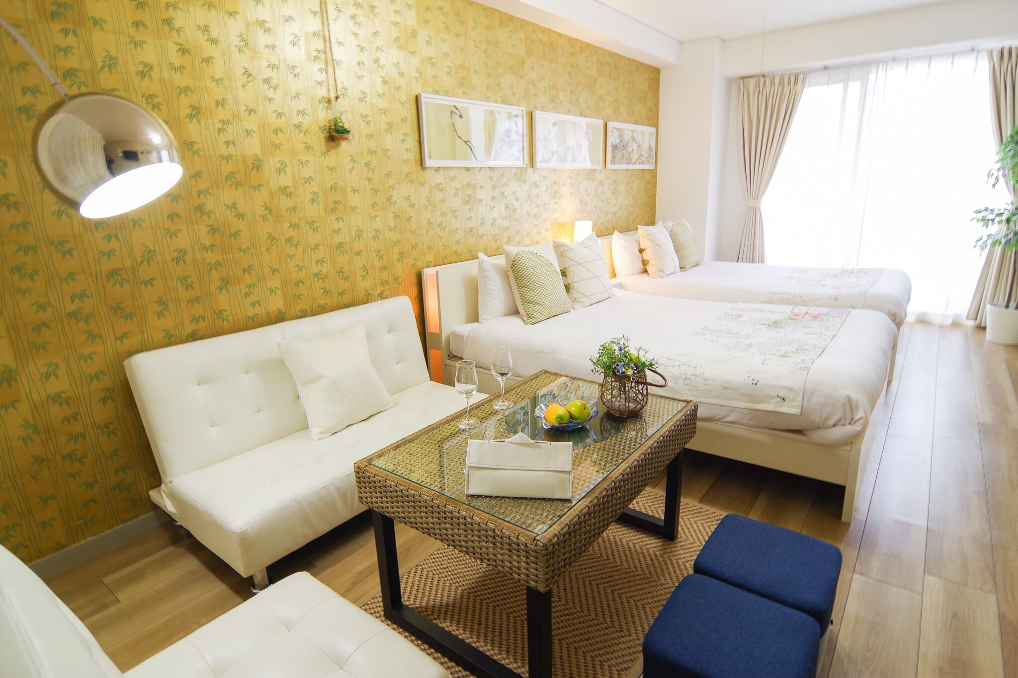A hotel room with a sofa, a bed, a glass coffee table, and a small table with a plant.