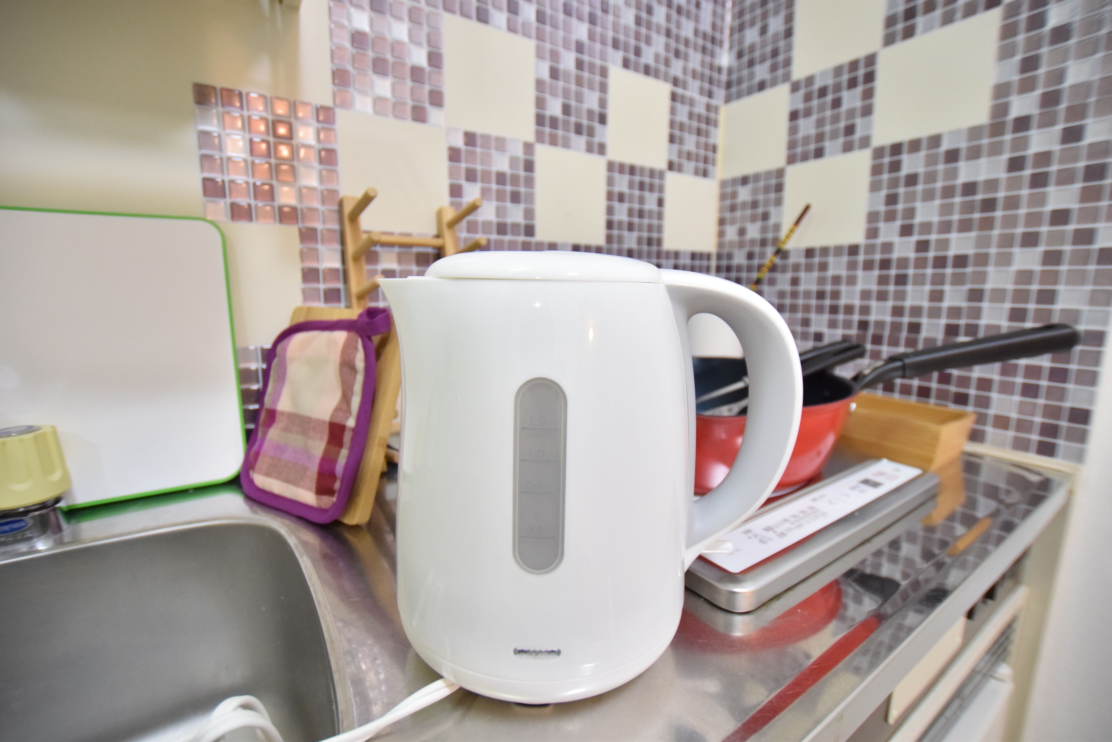 A kitchen counter with a white electric kettle, a red pot, and a measuring scale.