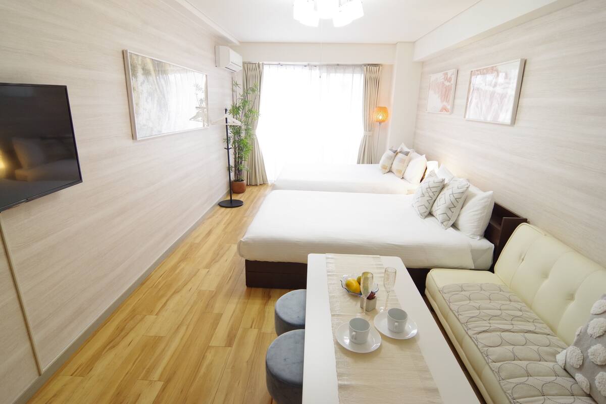 A hotel room with a bed, sofa, dining table, and a TV.
