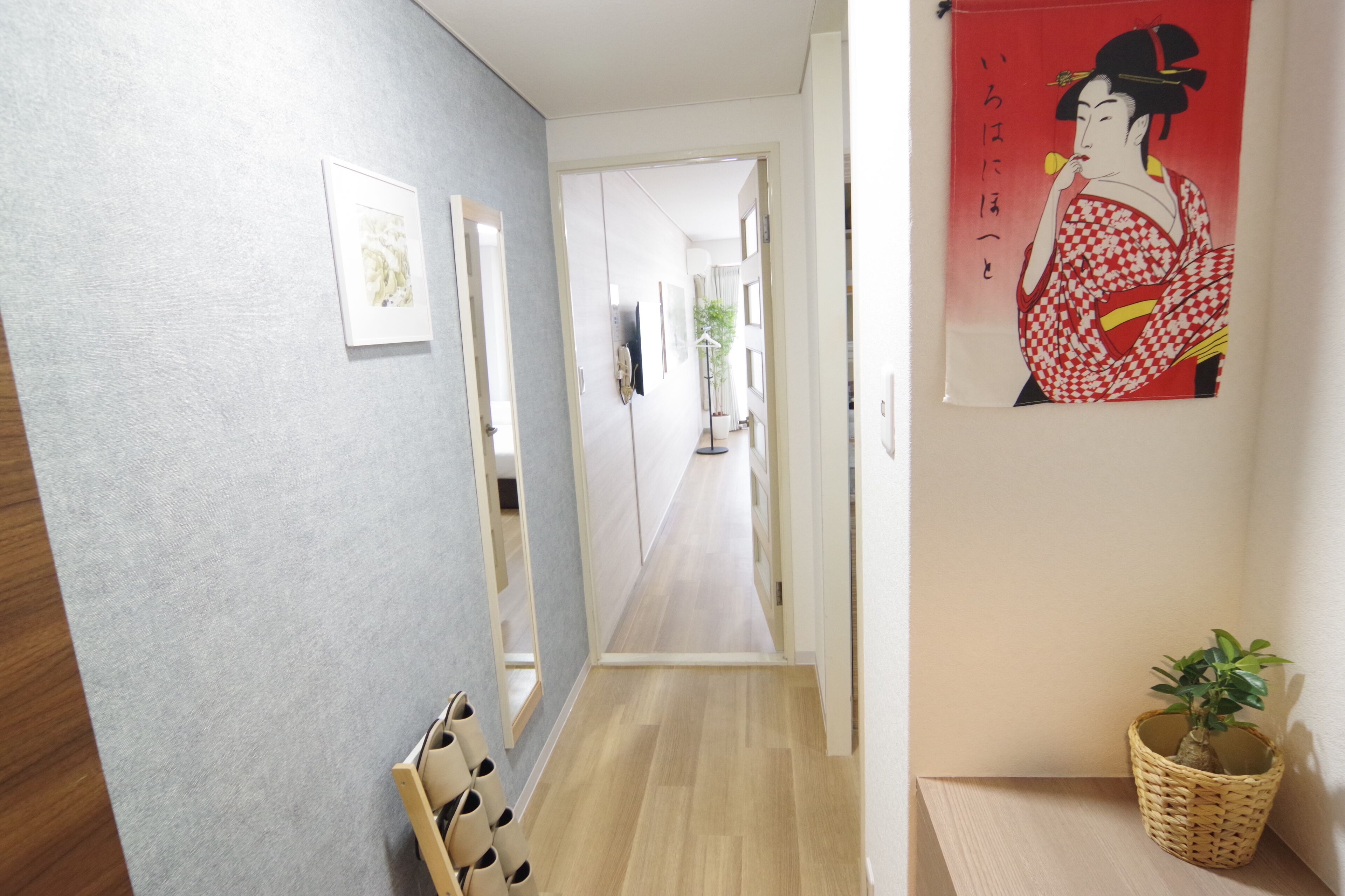 A hallway with a wooden floor, a mirror, a framed picture, and a poster on the wall.