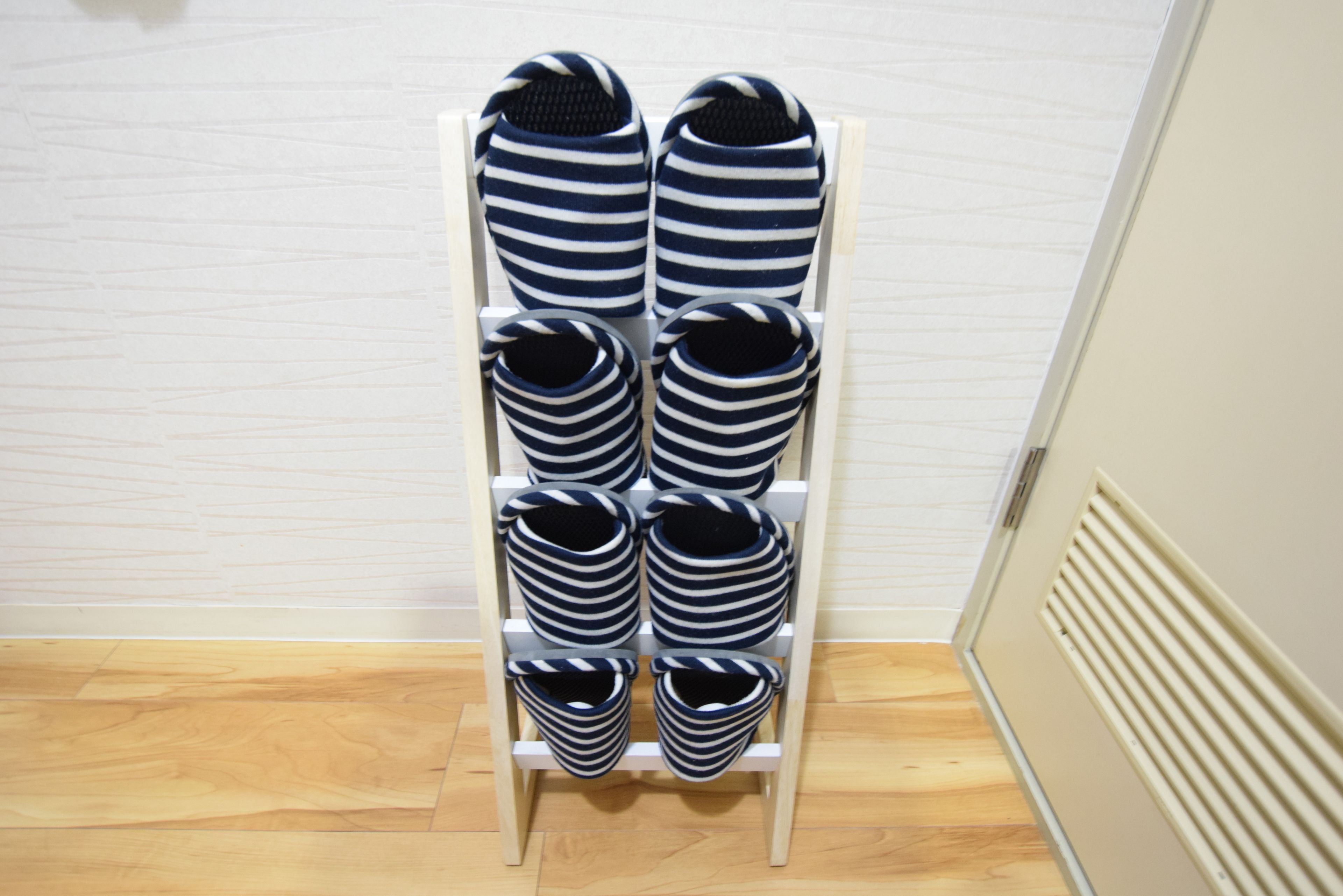 A white shoe rack with six pairs of striped slippers.