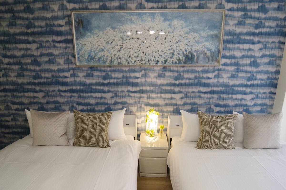A hotel room with two beds, a nightstand with a lamp, and a large painting on the wall.
