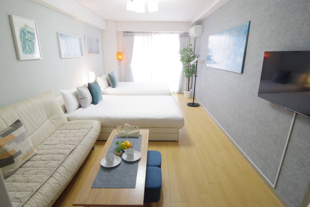A modern room with a sofa, a bed, a dining table with cups and fruits, and a TV.