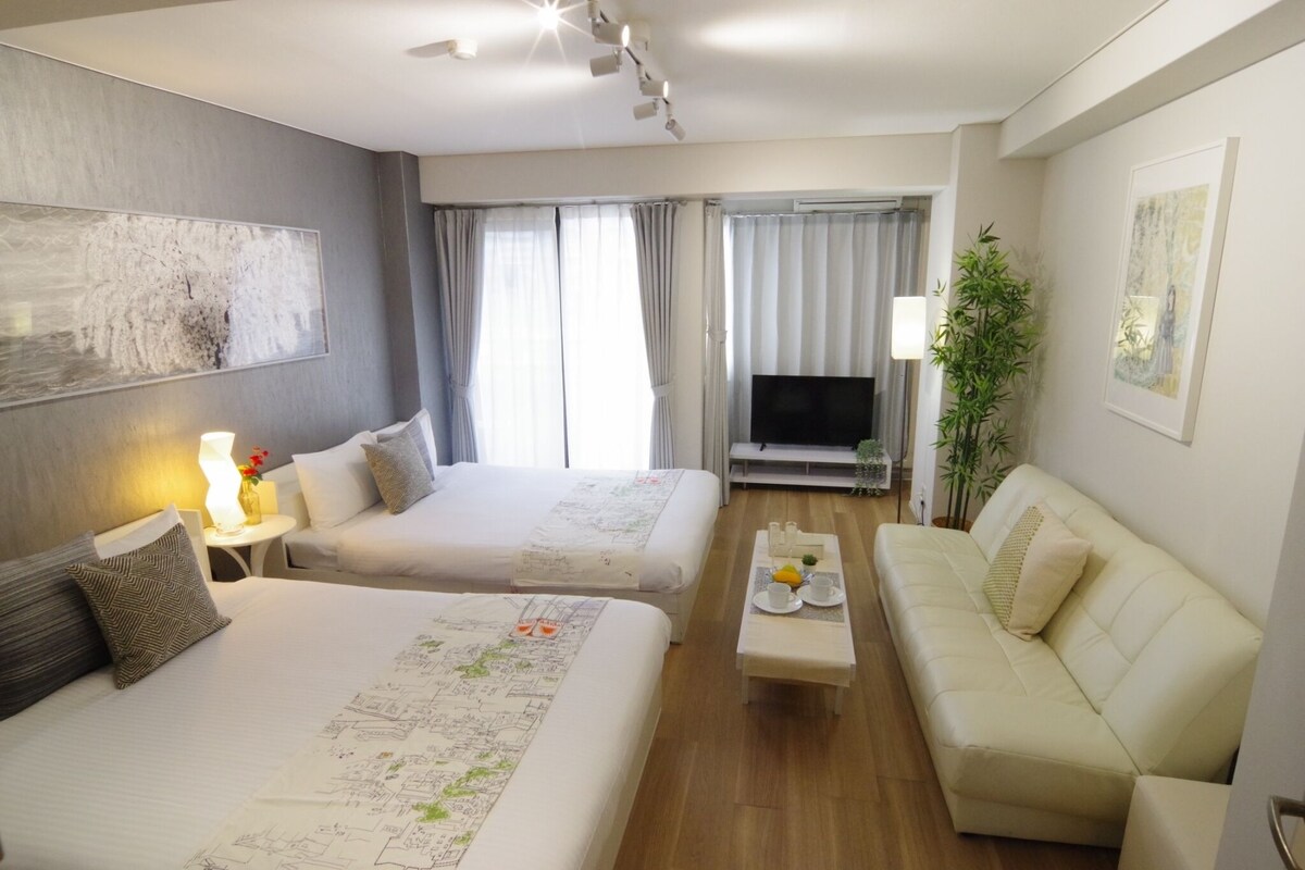 A hotel room with two beds, a sofa, a TV, and a dining table with breakfast items.