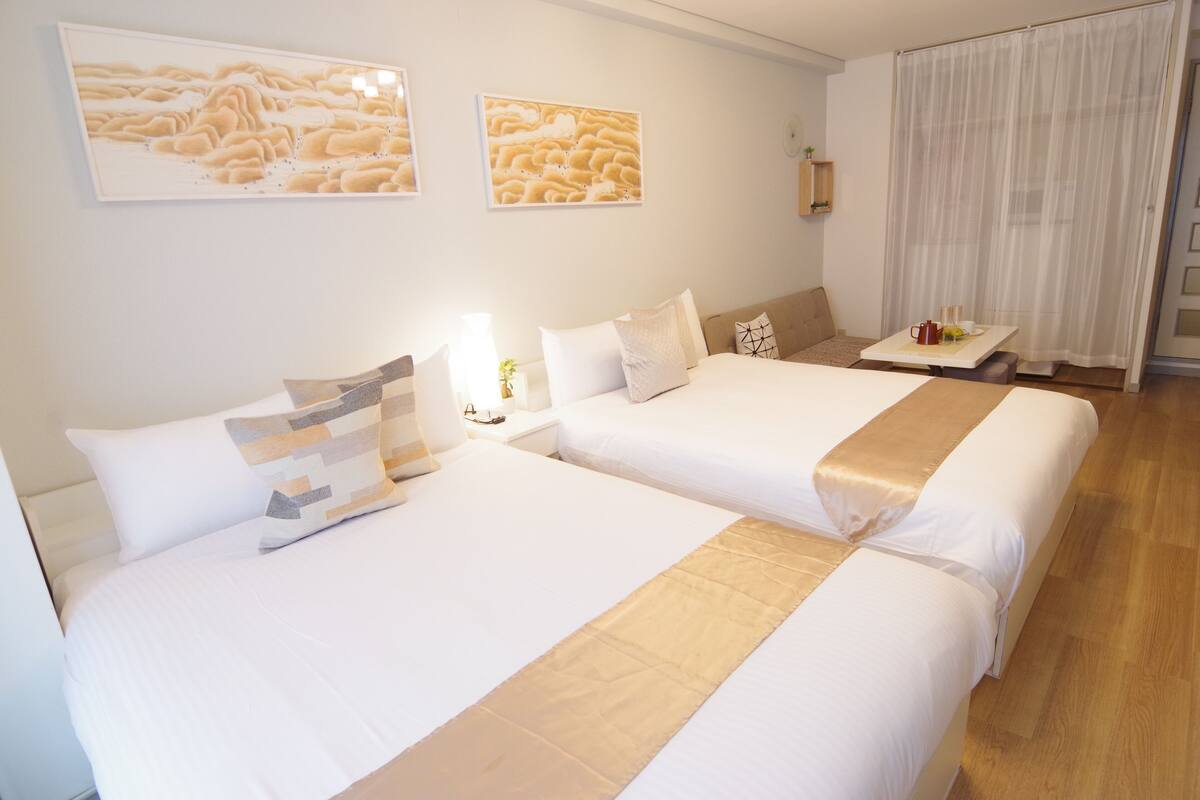 A hotel room with two beds, a bedside table with a lamp, and artwork on the wall.