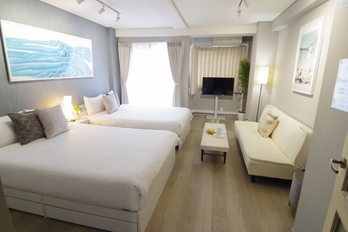 A hotel room with two beds, a sofa, a TV, and a small table with fruits.