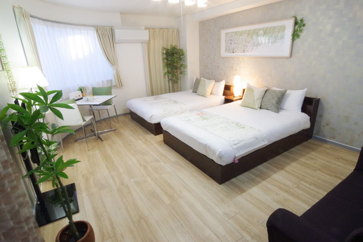 A hotel room with two beds, a desk, a chair, and a potted plant.