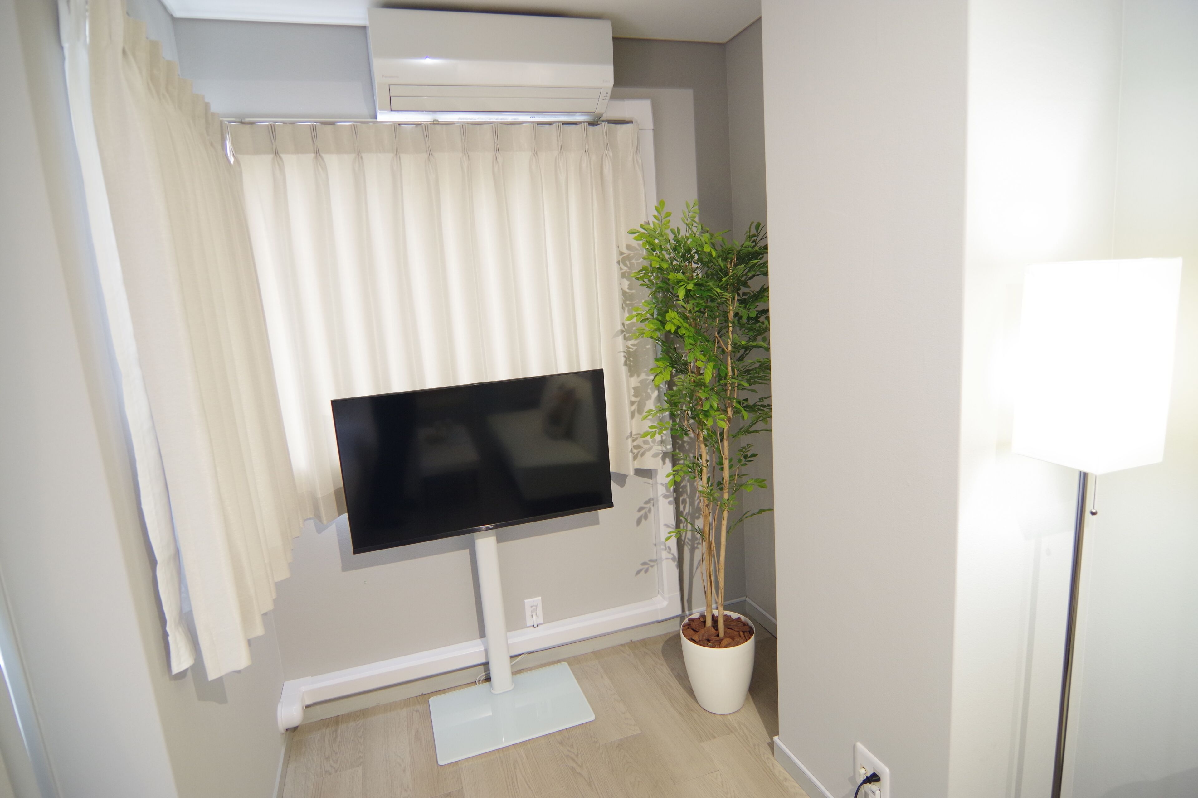 Een kamer met een wandgemonteerde flatscreen-tv, een potplant en een witte airconditioner boven de tv.