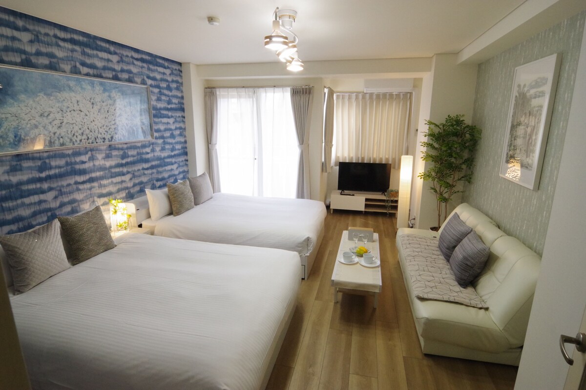 A hotel room with two beds, a TV, a sofa, a coffee table, and a large window with curtains.