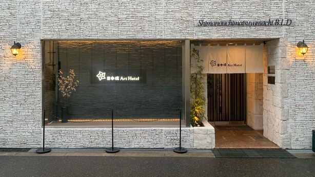 Eine Gebäudefassade mit steiniger Textur, ein großes Glasfenster mit dem Logo des Art Hotels und ein Schild über dem Eingang.