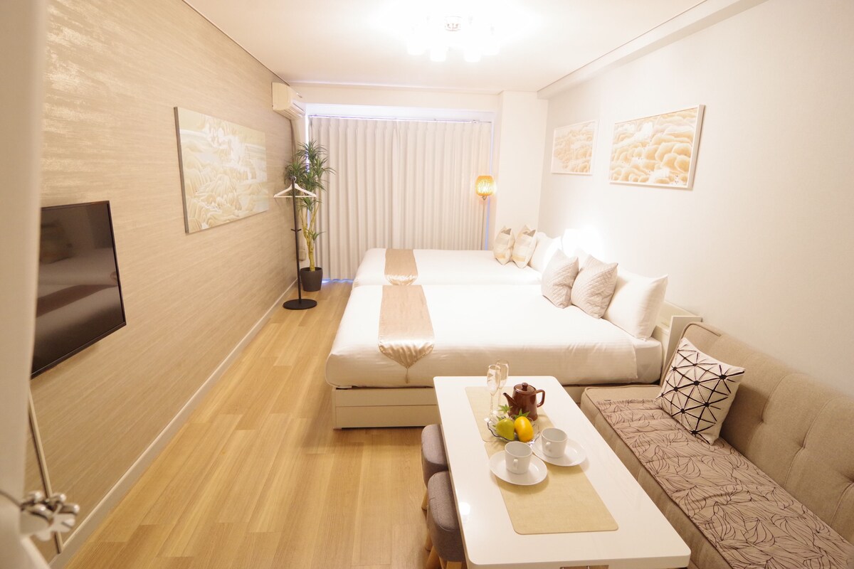 A modern hotel room with a bed, sofa, dining table, and artwork on the walls.