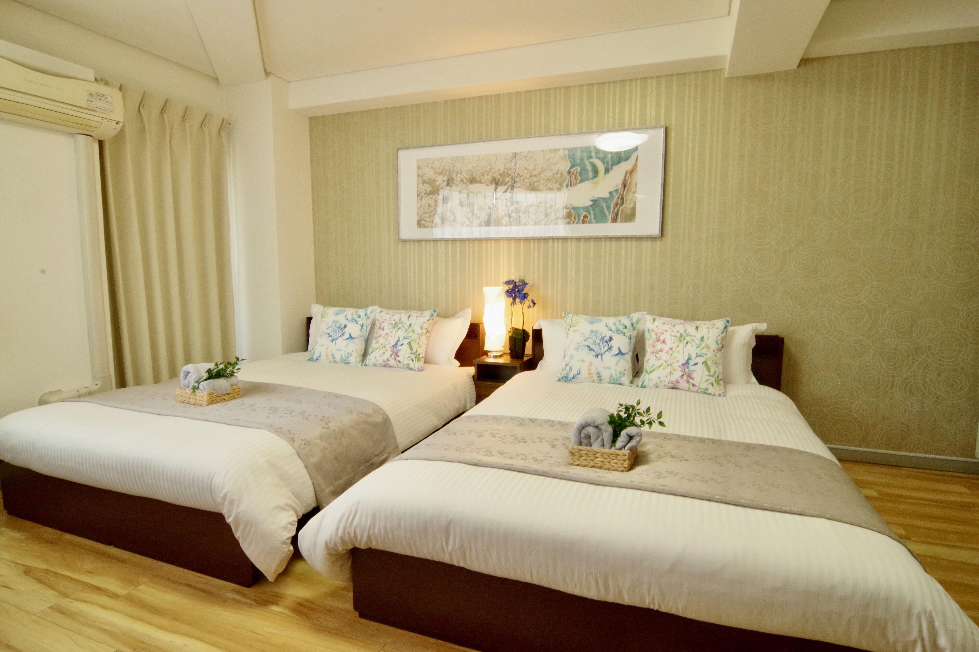 Habitación de hotel con dos camas, un ventanal con cortinas, una obra de arte en la pared y suelo de madera.