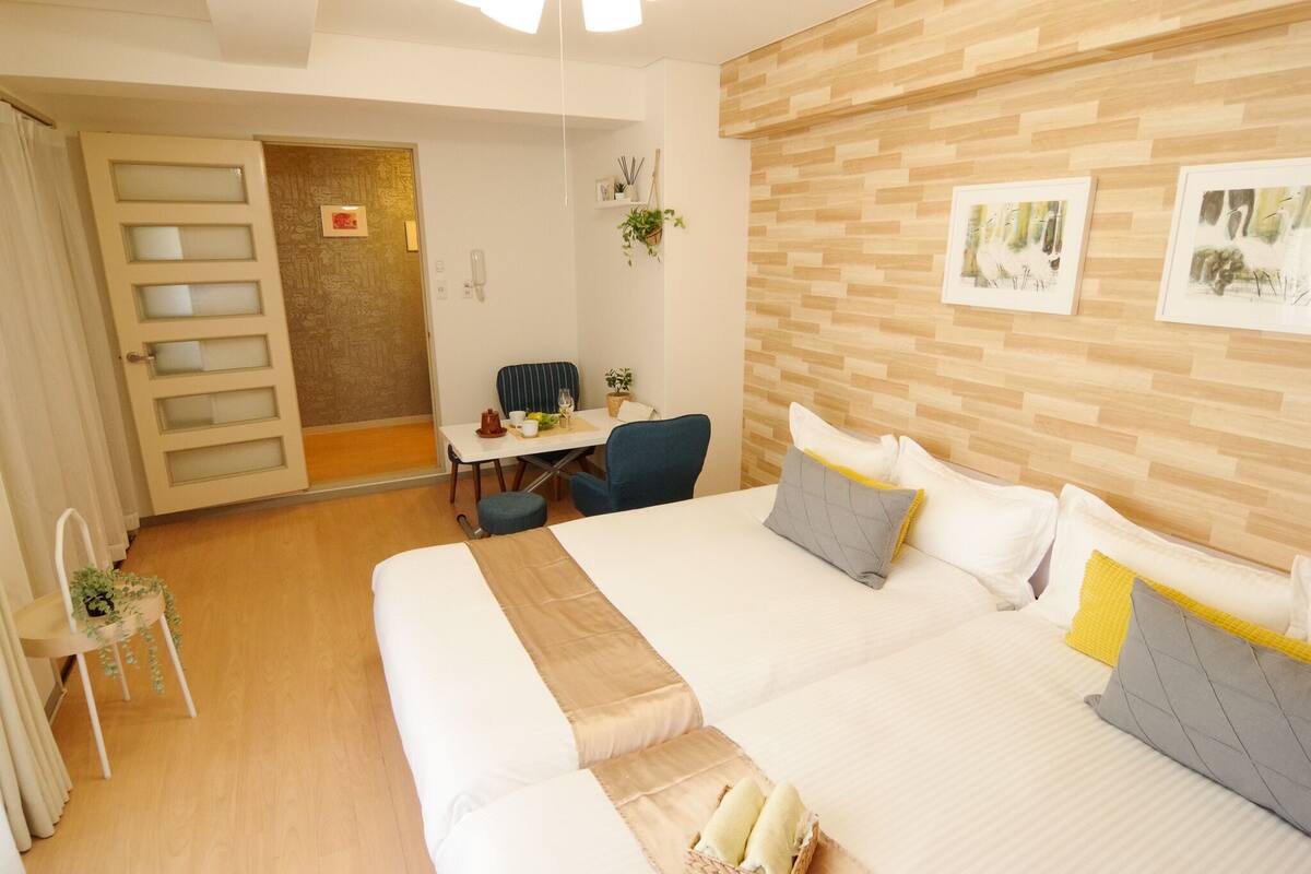 A hotel room with a large bed, a desk, and a chair. There is a door leading to another room and a wall with framed pictures.