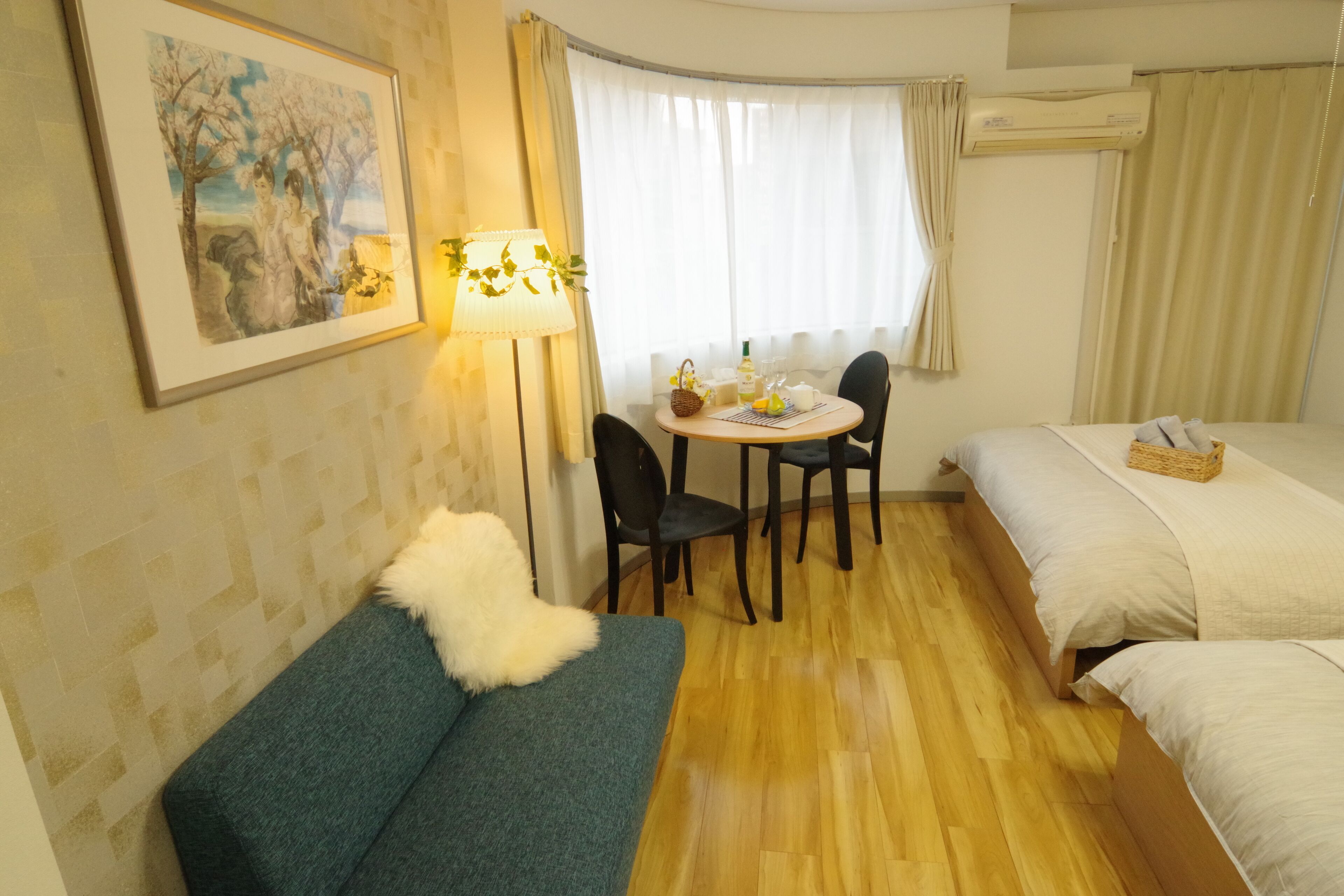 A hotel room with a bed, a sofa, a dining table with chairs, and a lamp.