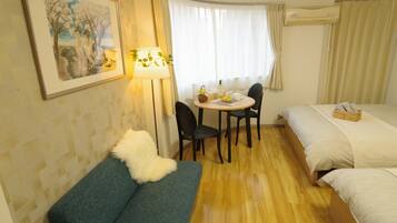 A hotel room with a bed, a sofa, a dining table with chairs, and a lamp.