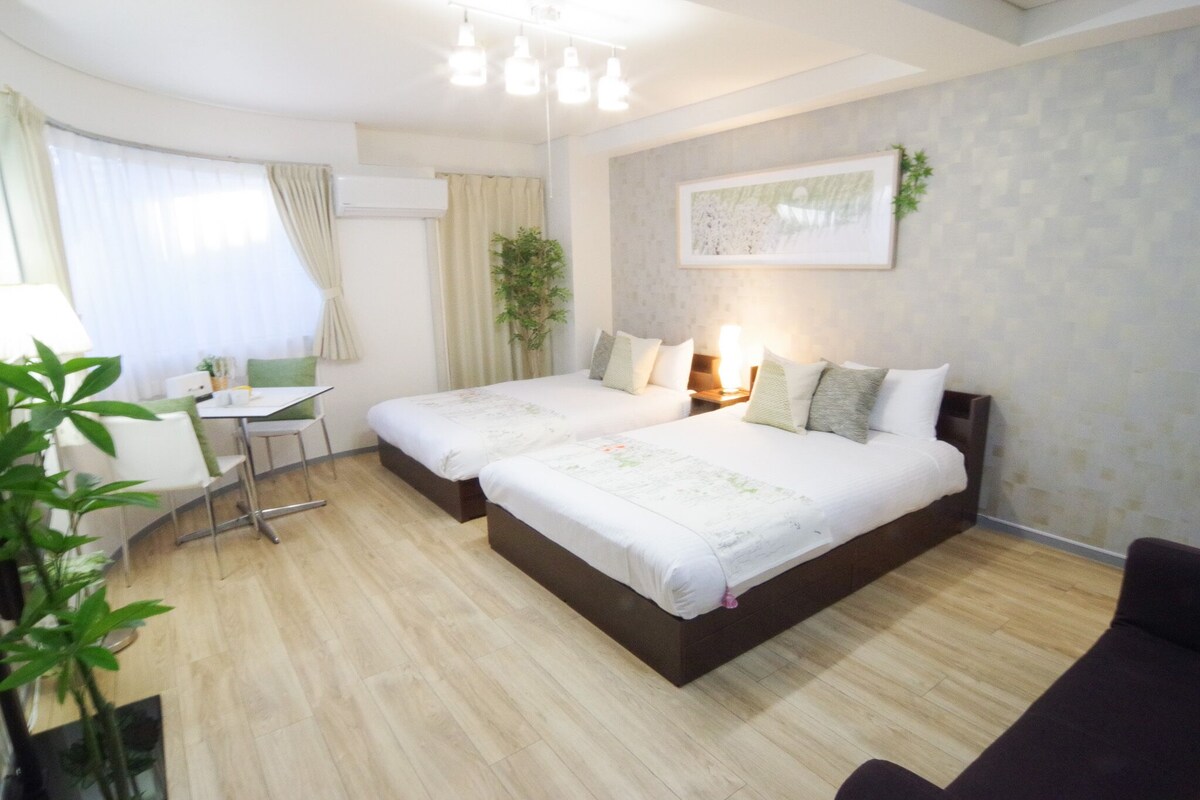 A hotel room with two beds, a desk, a chair, and a potted plant.