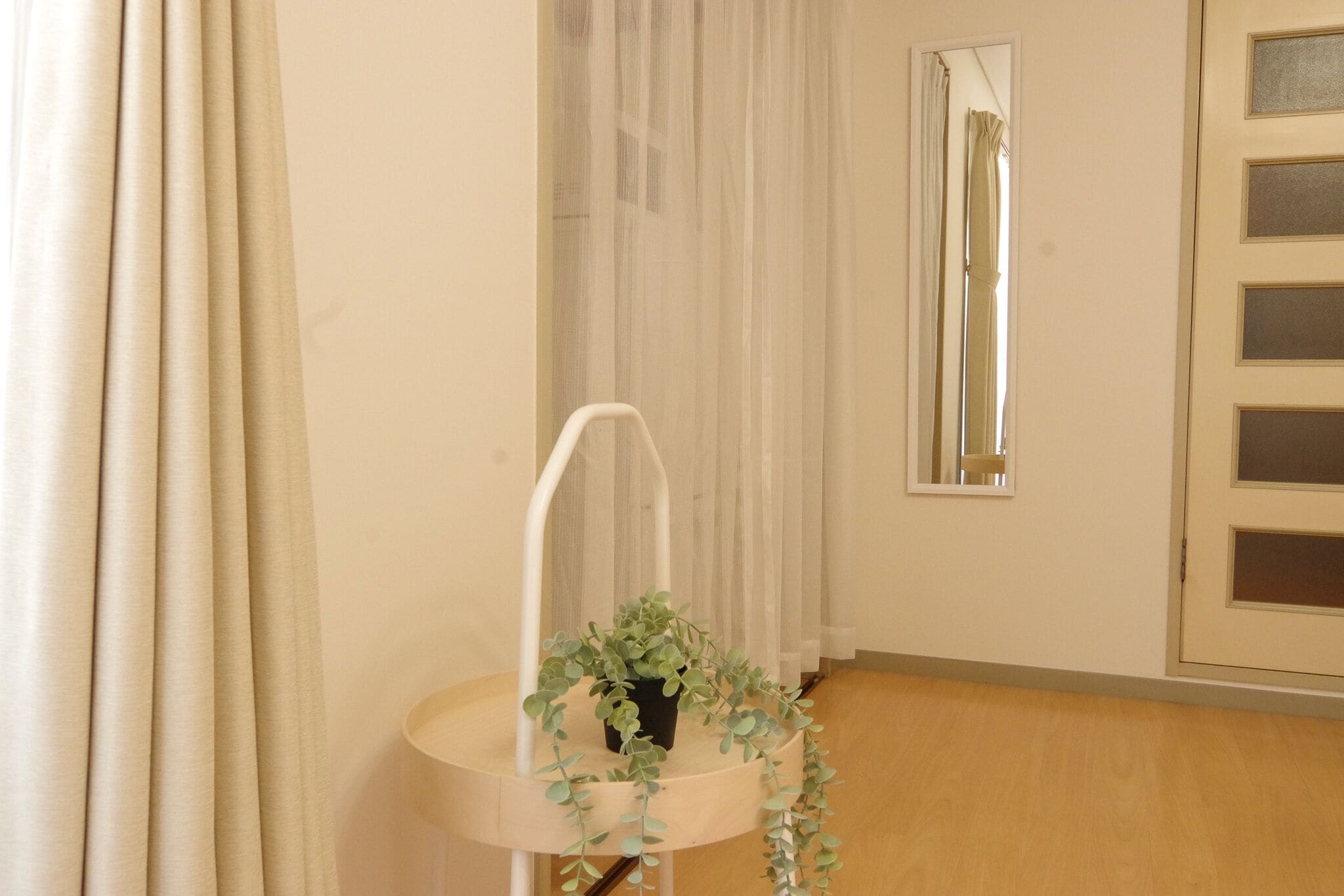 A room with a round wooden table, a potted plant, a white chair, a window with a mirror, and a door with glass panels.
