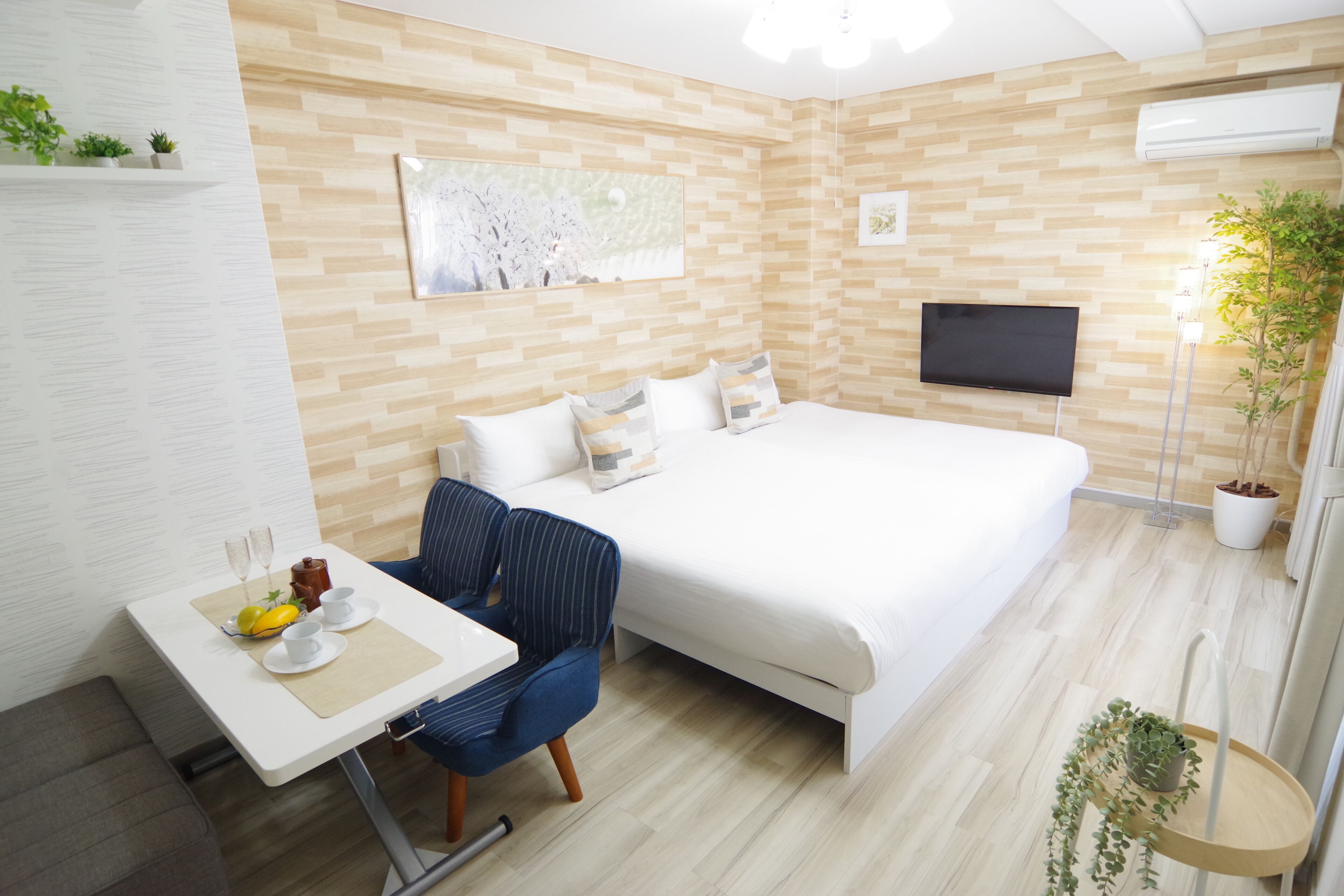 Camera d'albergo moderna con un letto grande, una TV a parete, un piccolo tavolo da pranzo con una sedia e una pianta in vaso.