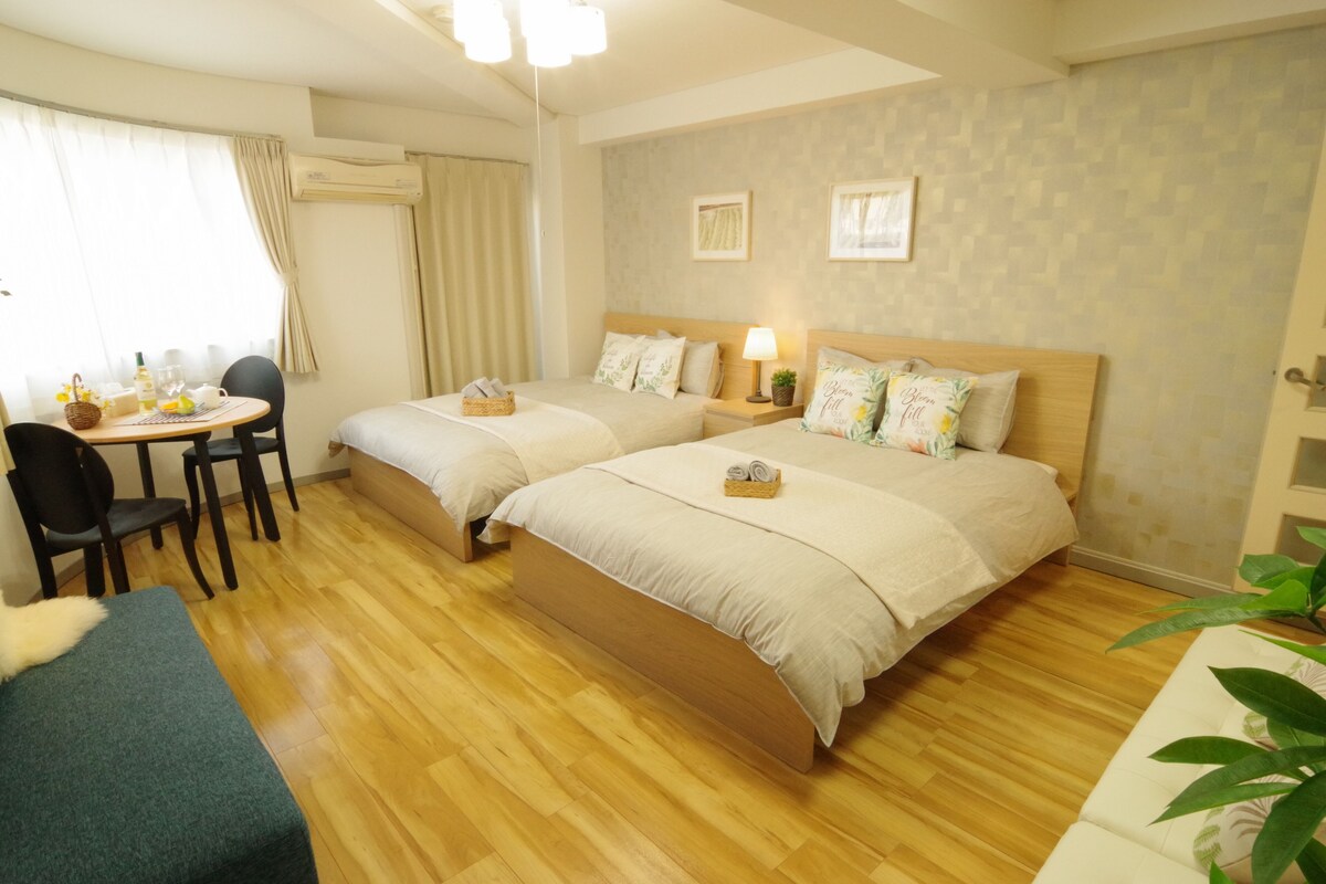 A hotel room with two beds, a small table with chairs, a sofa, and a potted plant.