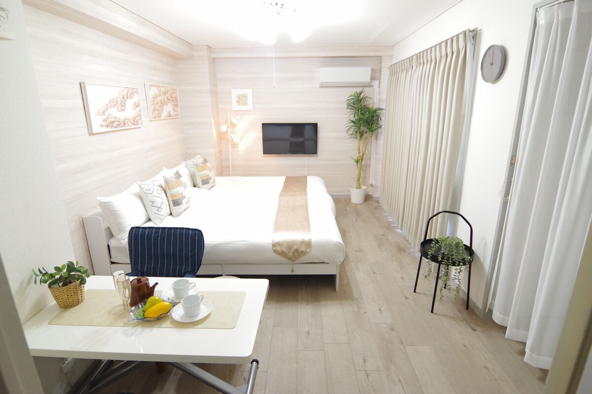 A hotel room with a bed, bedside table with breakfast items, a TV, and a potted plant.