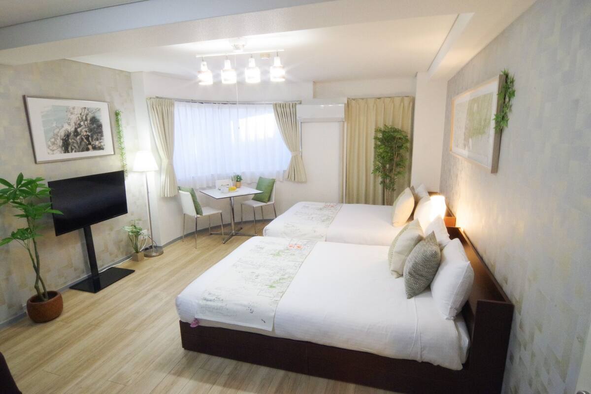 A hotel room with two beds, a desk, a chair, a TV, and a window with curtains.