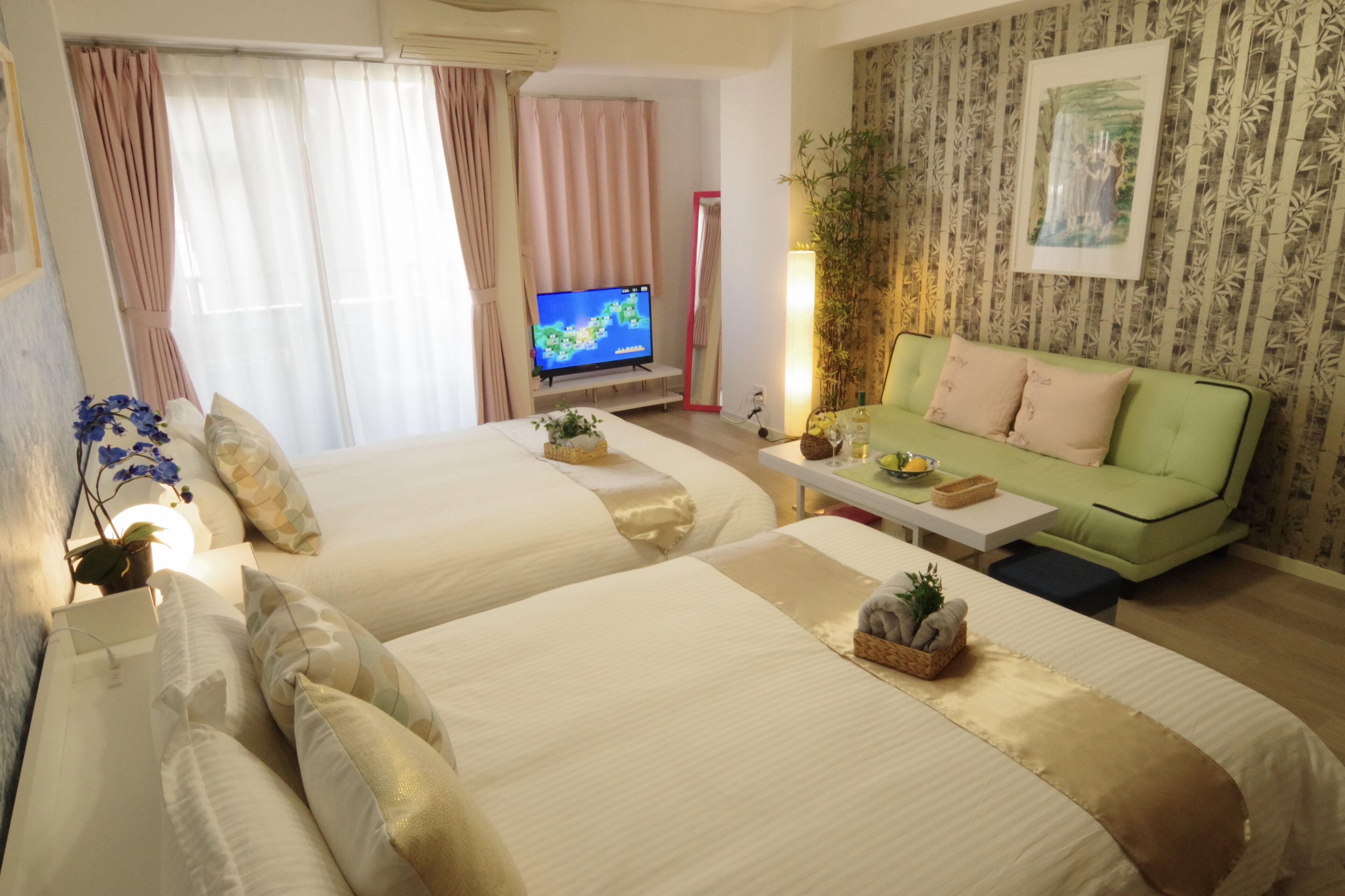 A hotel room with two beds, a green sofa, a television, and a mirror.