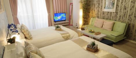 A hotel room with two beds, a green sofa, a television, and a mirror.