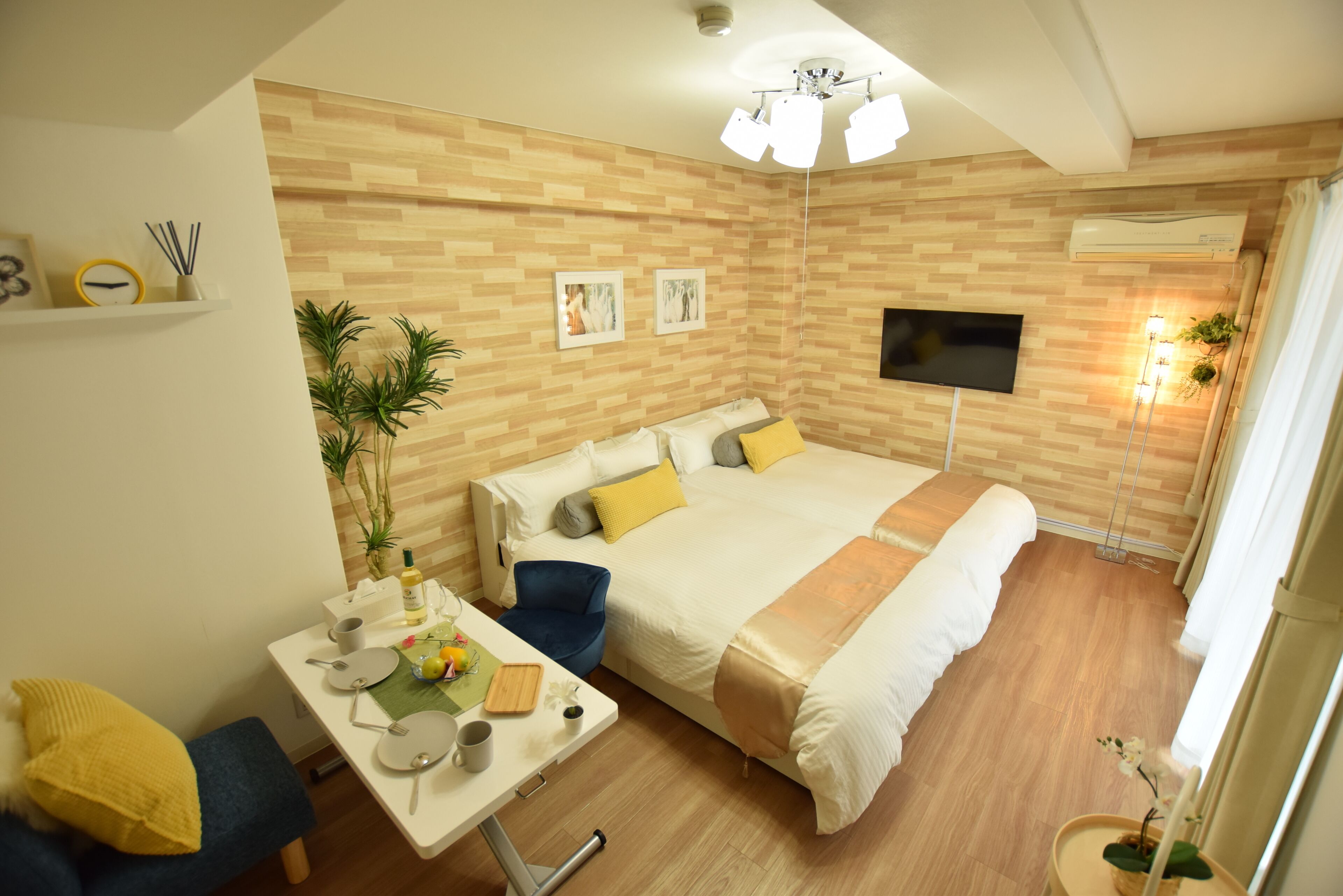 Una habitación de hotel moderna con una pared de madera, una cama con ropa de cama blanca y amarilla, un escritorio con una silla y un televisor montado en la pared.