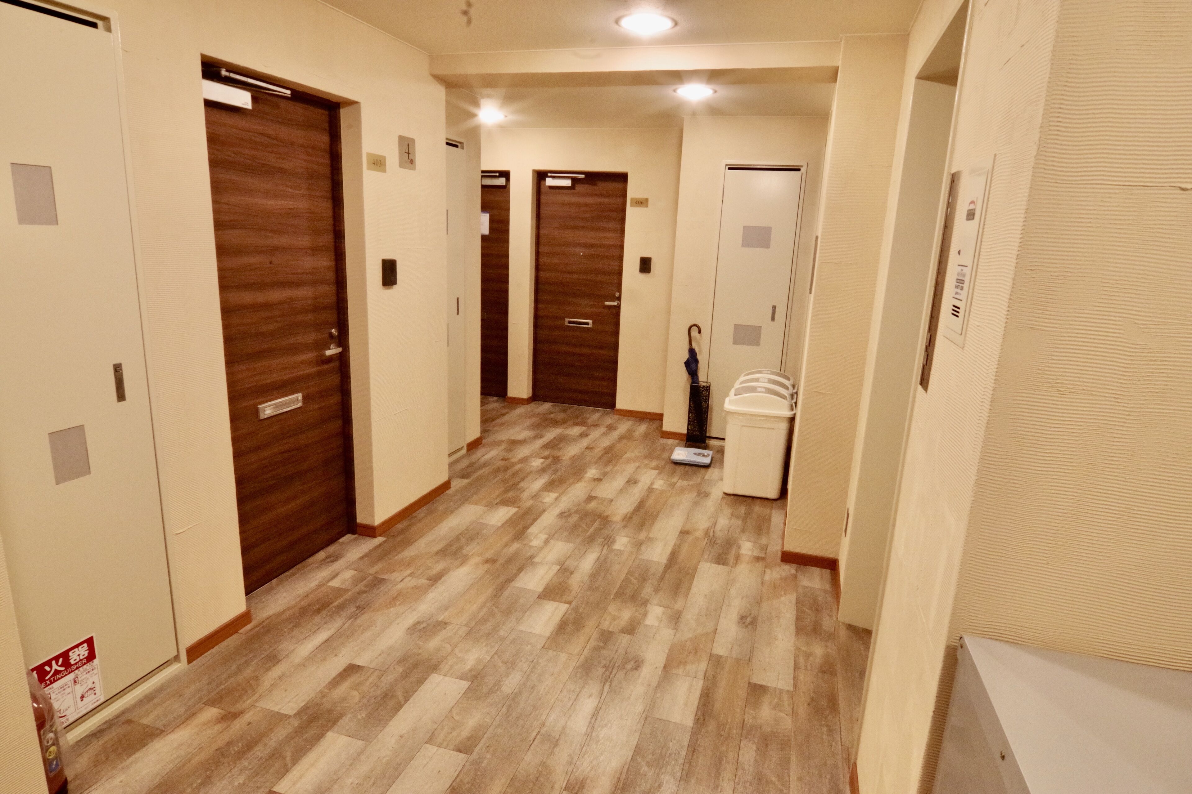 Pasillo de hotel con puertas de madera, una balanza y un cubo de basura.
