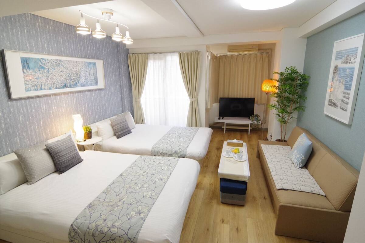 A hotel room with two beds, a TV, a sofa, and a dining table with a plant.