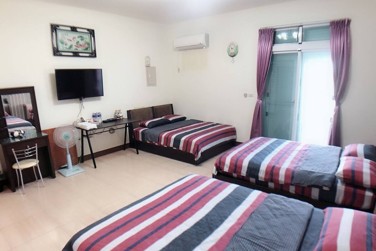 Habitación de hotel con dos camas individuales, un escritorio con silla, televisor, aire acondicionado y ventana con cortinas.