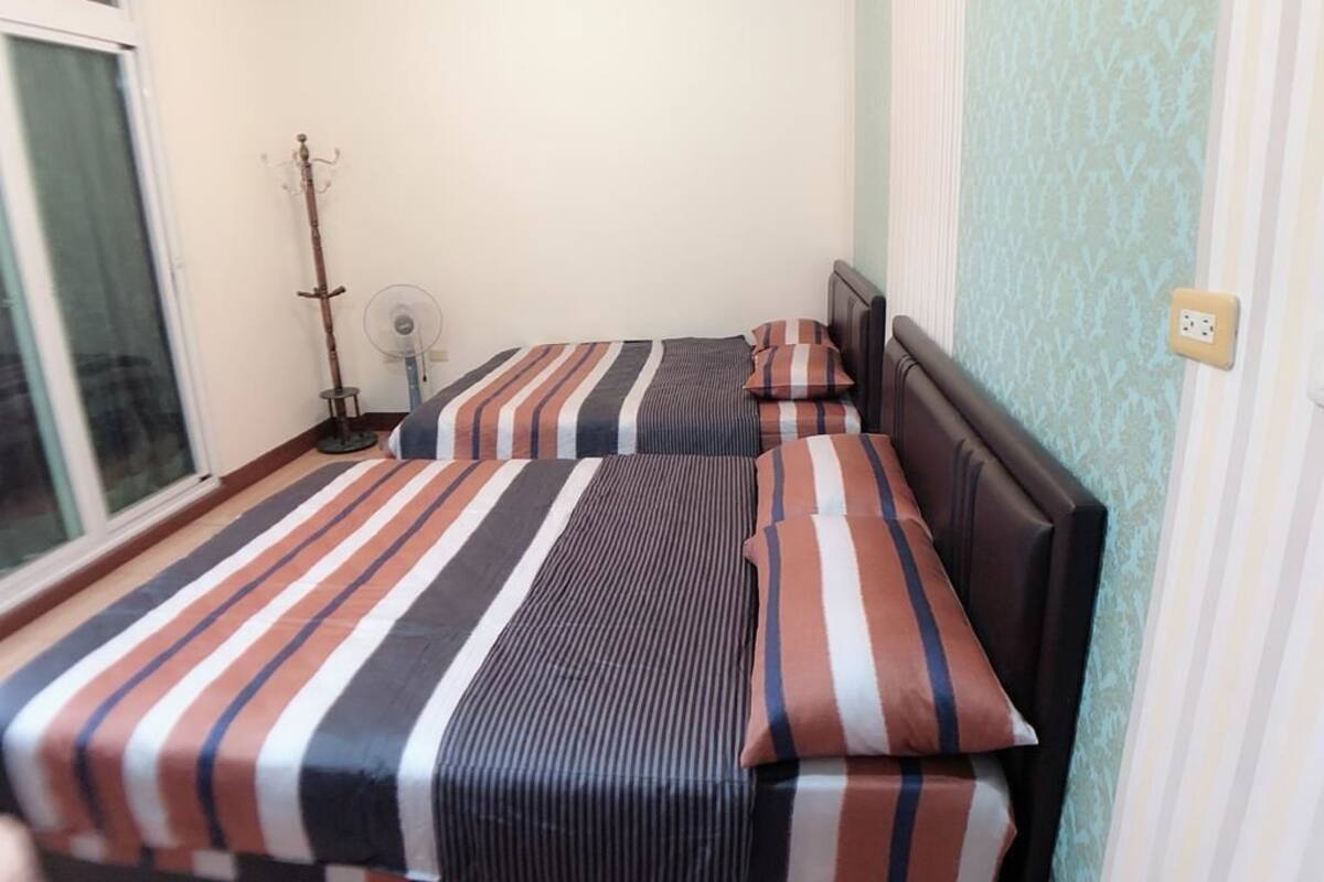 Una habitación con una cama con ropa de cama a rayas, una mesita de noche y una ventana.