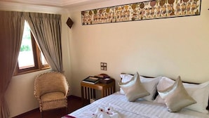 A hotel room with a bed, a chair, a small table with books, and a decorative wall piece. - WEStay at Boutique House Bagan (Nyaung-U)