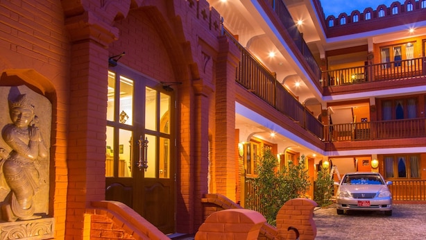 A hotel with a traditional architectural style, featuring a courtyard with a statue, a car parked outside, and a double-story building with balconies. - WEStay at Boutique House Bagan (Nyaung-U)