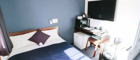 A hotel room with a bed, a desk, a microwave, a TV, and a small refrigerator.