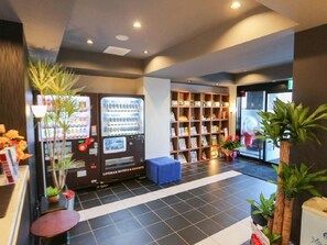 A hotel lobby with vending machines, a bookshelf, and a seating area. - Hotel LiVEMAX Machida-Ekimae (Machida)