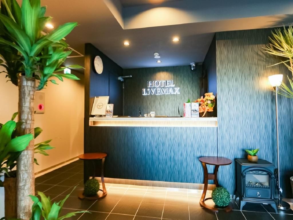 Zona de recepción de un hotel con un mostrador, un reloj y un cartel que dice 'HOTEL LIVEMAX'.