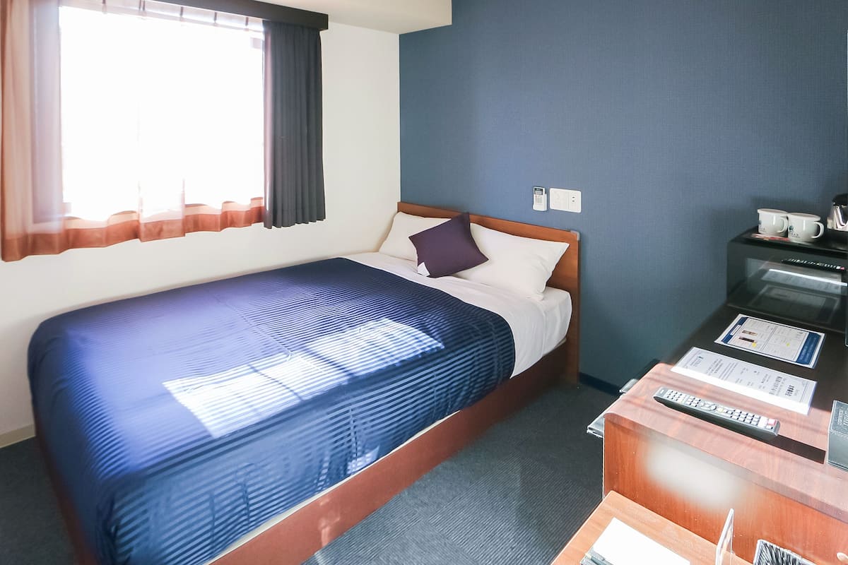 A hotel room with a bed, a desk, a coffee machine, and a window with curtains.