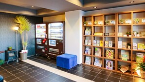 Ein Empfangsbereich mit einem Verkaufsautomaten, einer blauen Bank und einem Bücherregal mit verschiedenen Gegenständen.