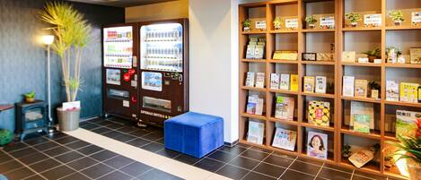 A reception area with a vending machine, a blue bench, and a bookshelf with various items.