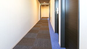 Ein Hotelgang mit Teppichboden, einer dunklen Holztür rechts und einer hellen Wand links.