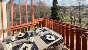 Un balcon avec une table dressée pour deux, une vue sur les arbres et un paysage lointain, et un ciel dégagé.
