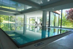 Ein moderner, überdachter Pool mit Glaswänden, Fliesenboden und Blick ins Freie.