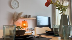 Une table à manger élégamment dressée, agrémentée d’un vase de fleurs, d’une horloge et d’un téléviseur en arrière-plan.