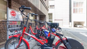 A row of red bicycles parked outside a building with a sign indicating a hotel. - Hotel Livemax BUDGET Shimbashi (Tokyo)