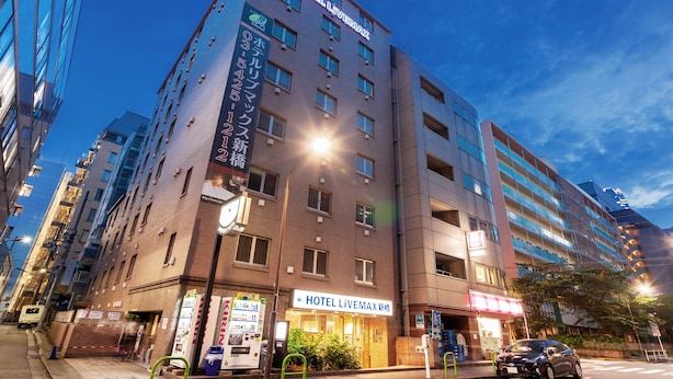 A multi-story hotel with a prominent 'HOTEL LIVEMAX' sign, a visible entrance, vending machines, and a parking area with a car. - Hotel Livemax BUDGET Shimbashi (Tokyo)